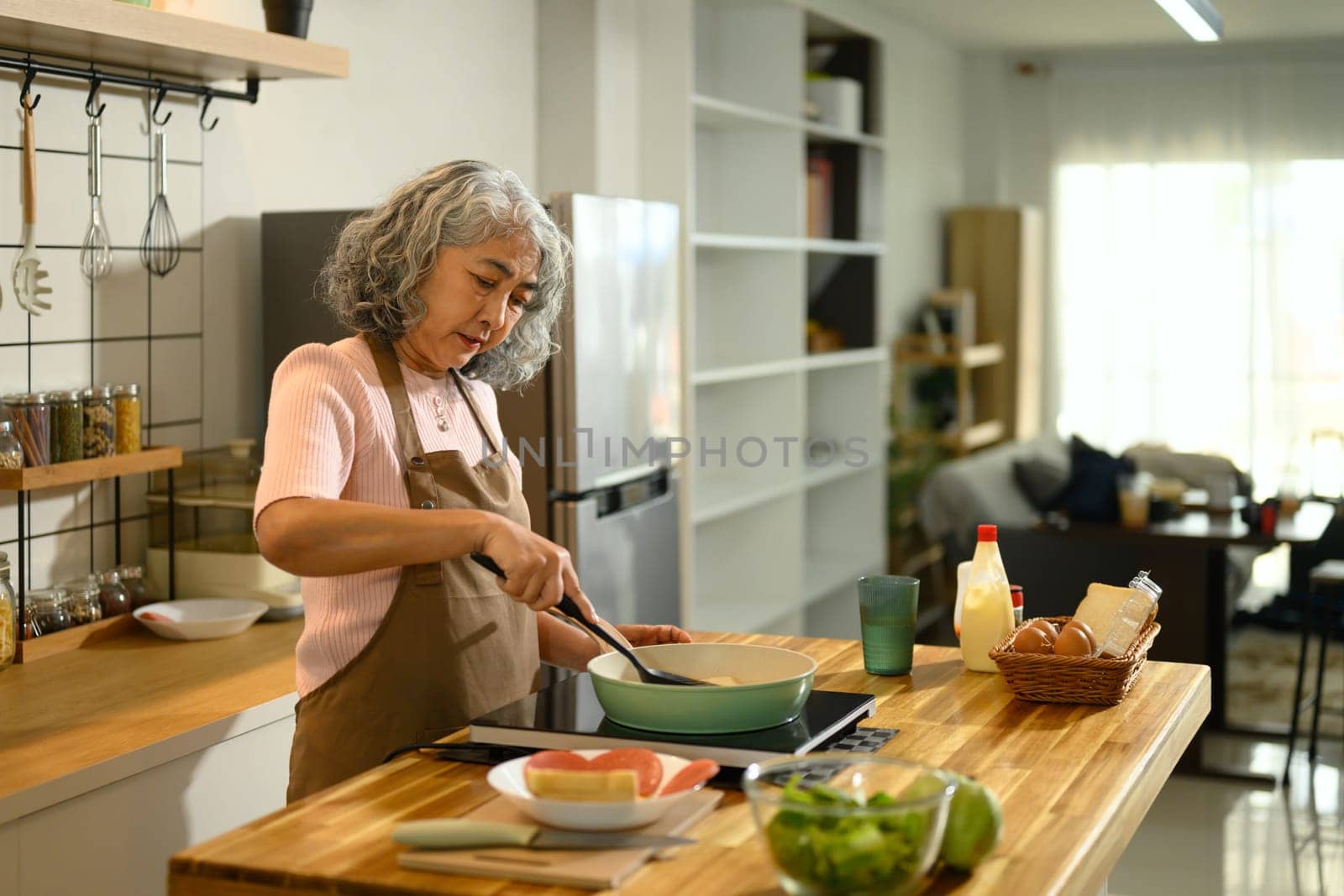 Senior woman wearing apron preparing breakfast in a stylish kitchen.