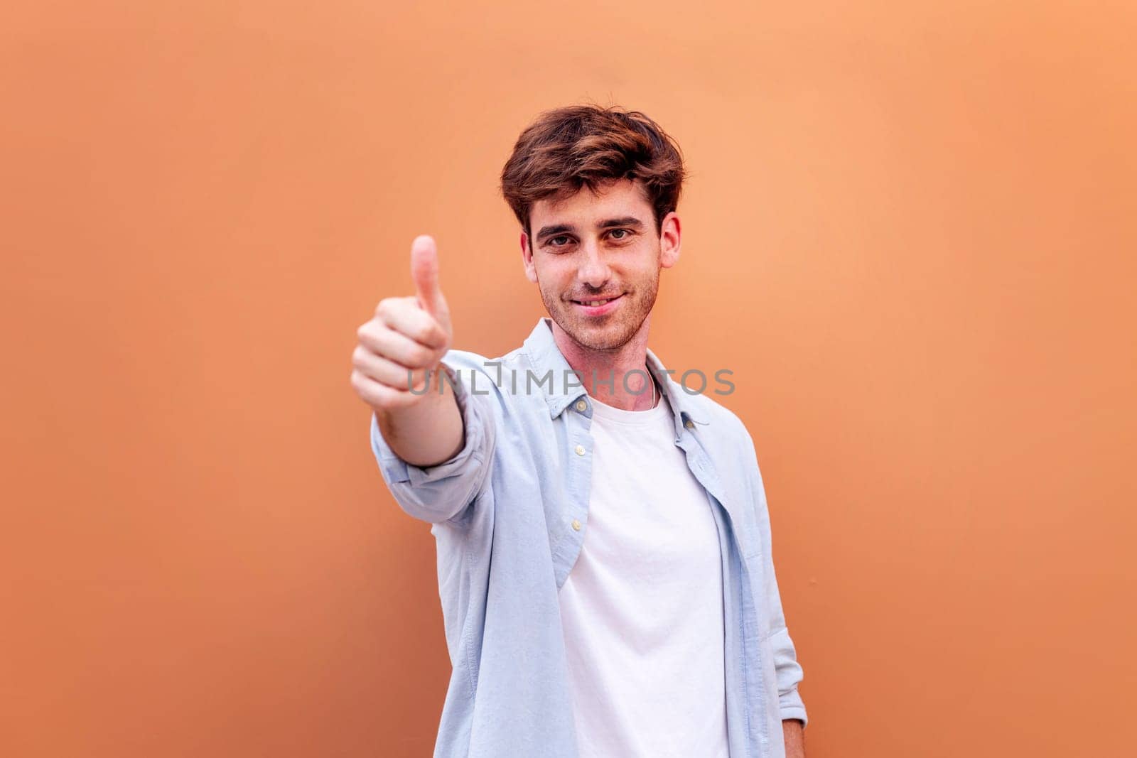 young man giving a thumb up gesture while smiling looking at camera in a positive and friendly mood suggesting that he is happy and content, copyspace for text