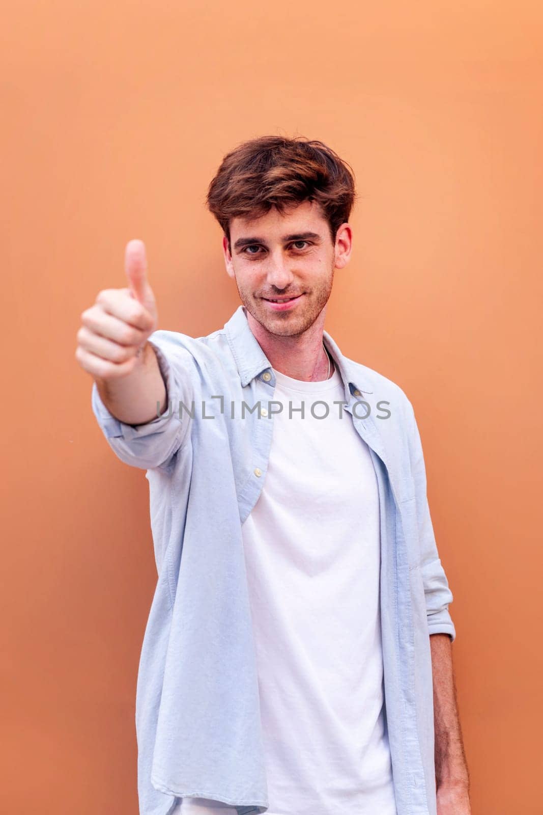 young man giving a thumb up gesture while smiling looking at camera in a positive and friendly mood suggesting that he is happy and content, copyspace for text