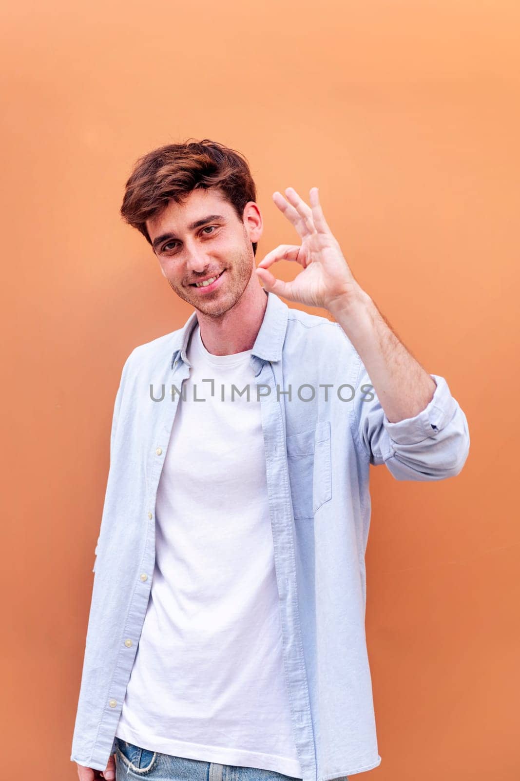 young man doing ok sign with hand while smiling looking at camera in a positive and friendly mood suggesting that he is happy and content, copyspace for text