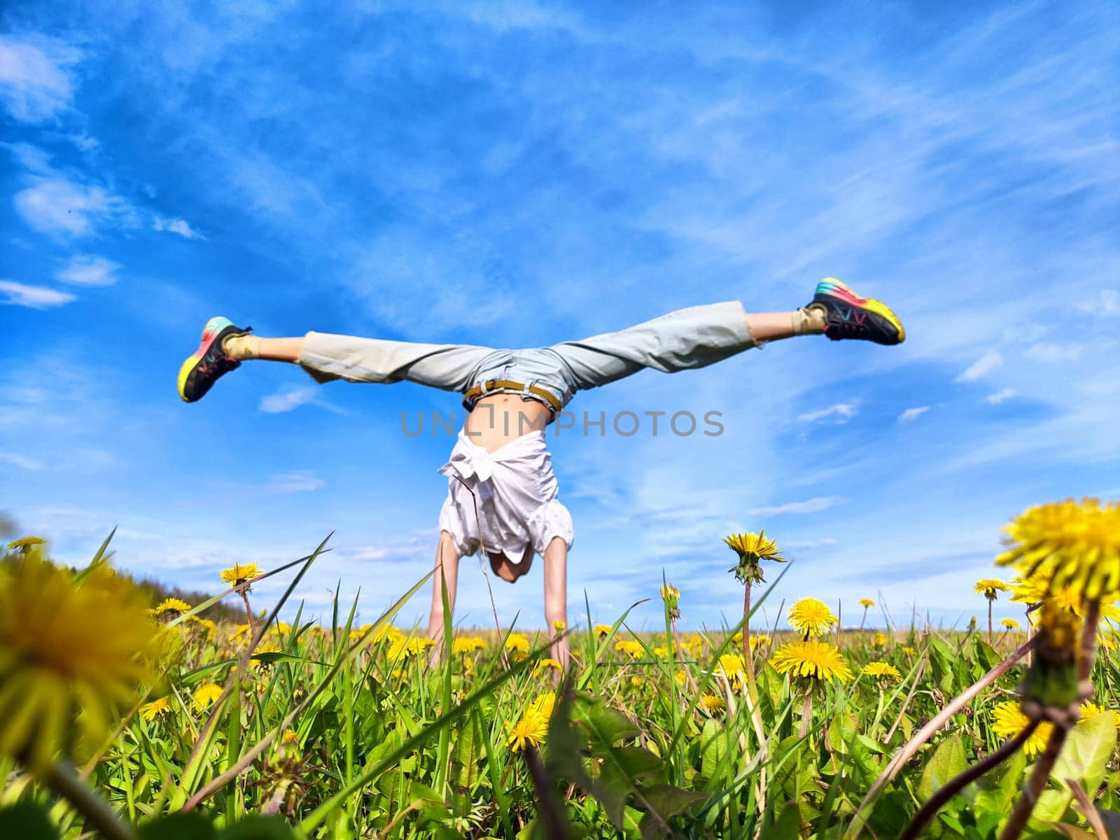 A person performs a handstand in a vibrant field of dandelions, enjoying the sunny weather and clear blue sky above.