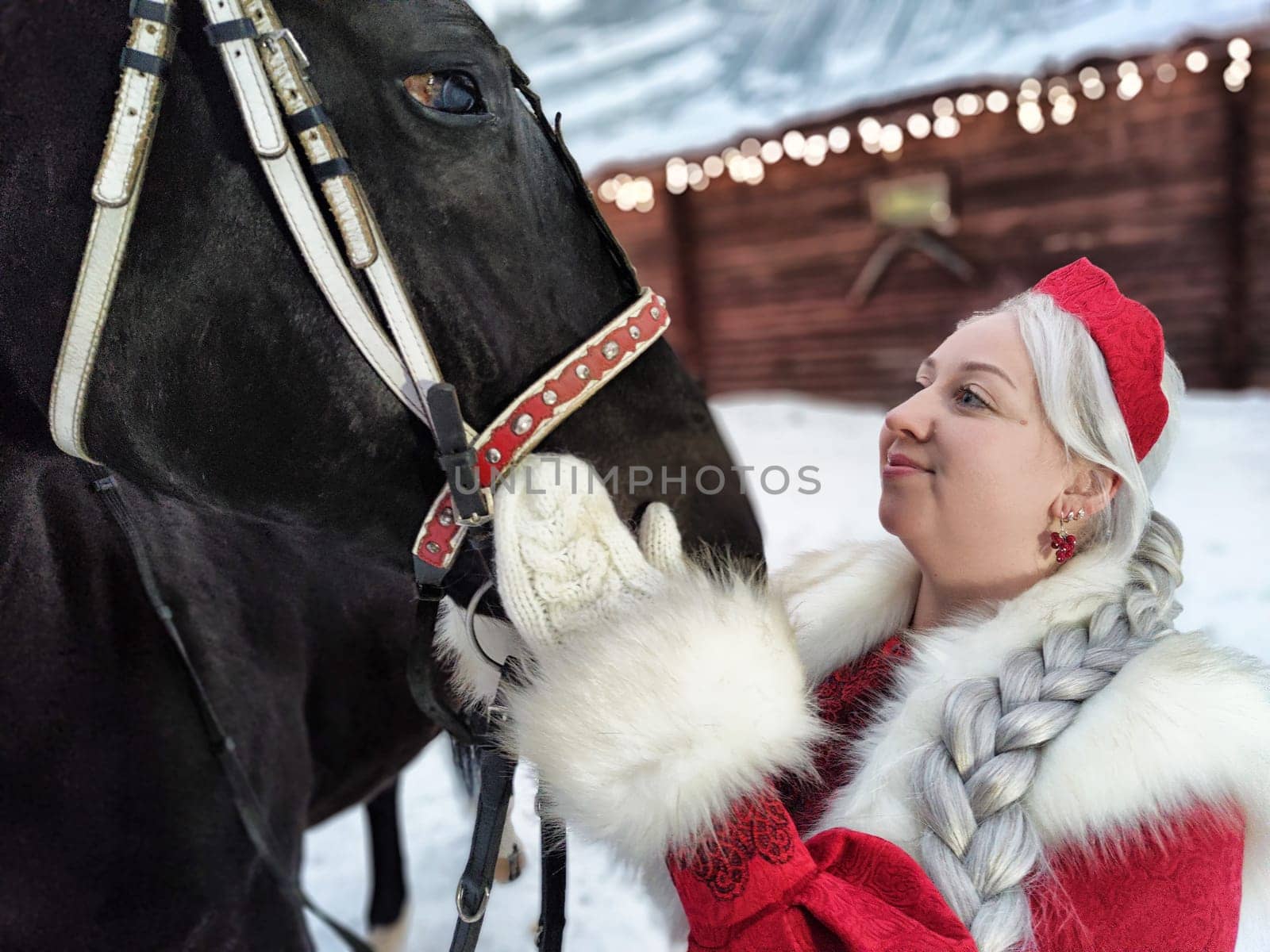 A girl in a national dress interacts with a horse in a winter setting, celebrating the Maslenitsa festival.