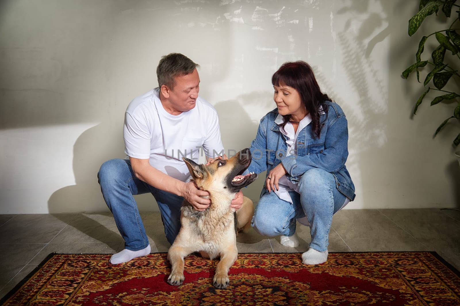 A loving middle-aged couple enjoys quality time with their german shepherd in their stylish apartment, showcasing their close bond and happiness.