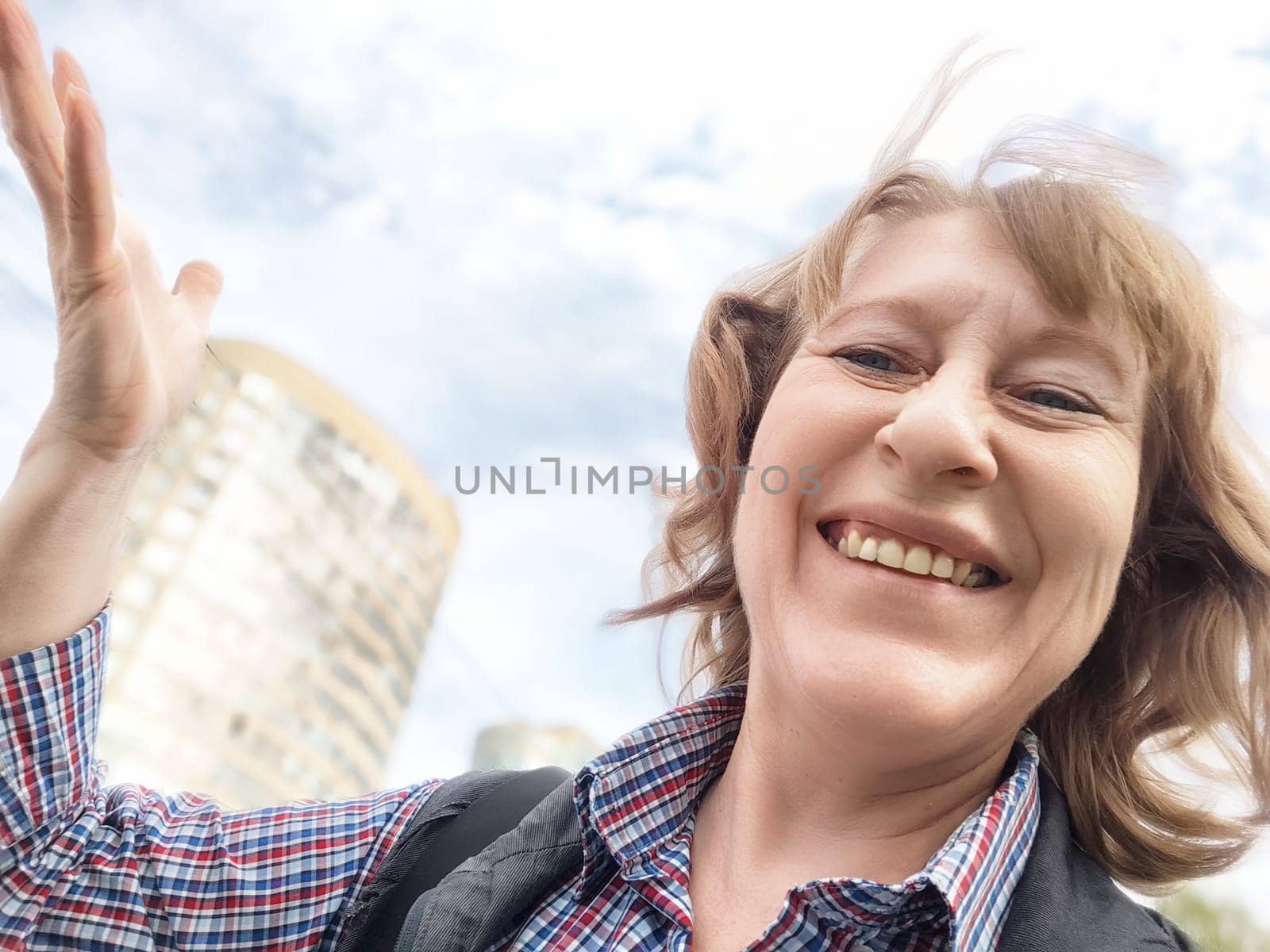 A middle-aged woman captures a joyful moment with a selfie during her summer trip in a lively city atmosphere.