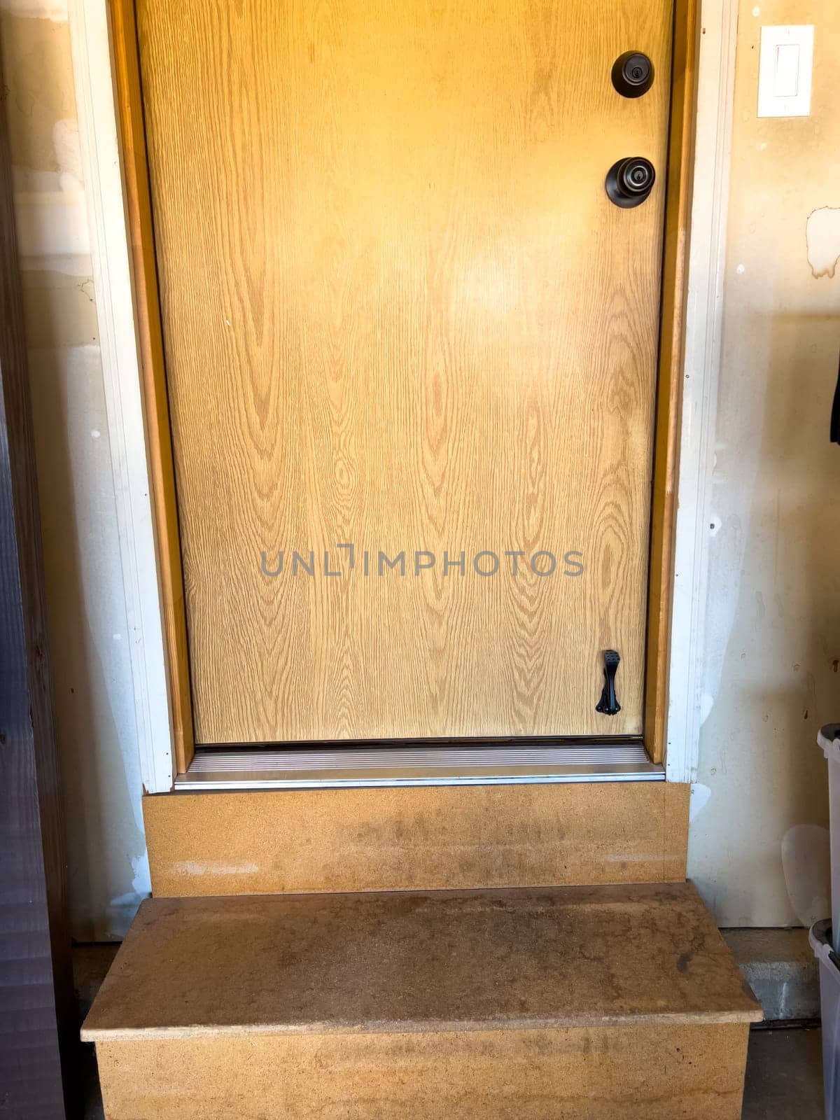 Broomfield, Colorado, USA-February 23, 2025-A wooden interior door leading from the garage into the home, featuring a small step for entry. The door has a natural wood finish with a black handle and deadbolt. Surrounding the door is a beige-painted wall with visible signs of wear.