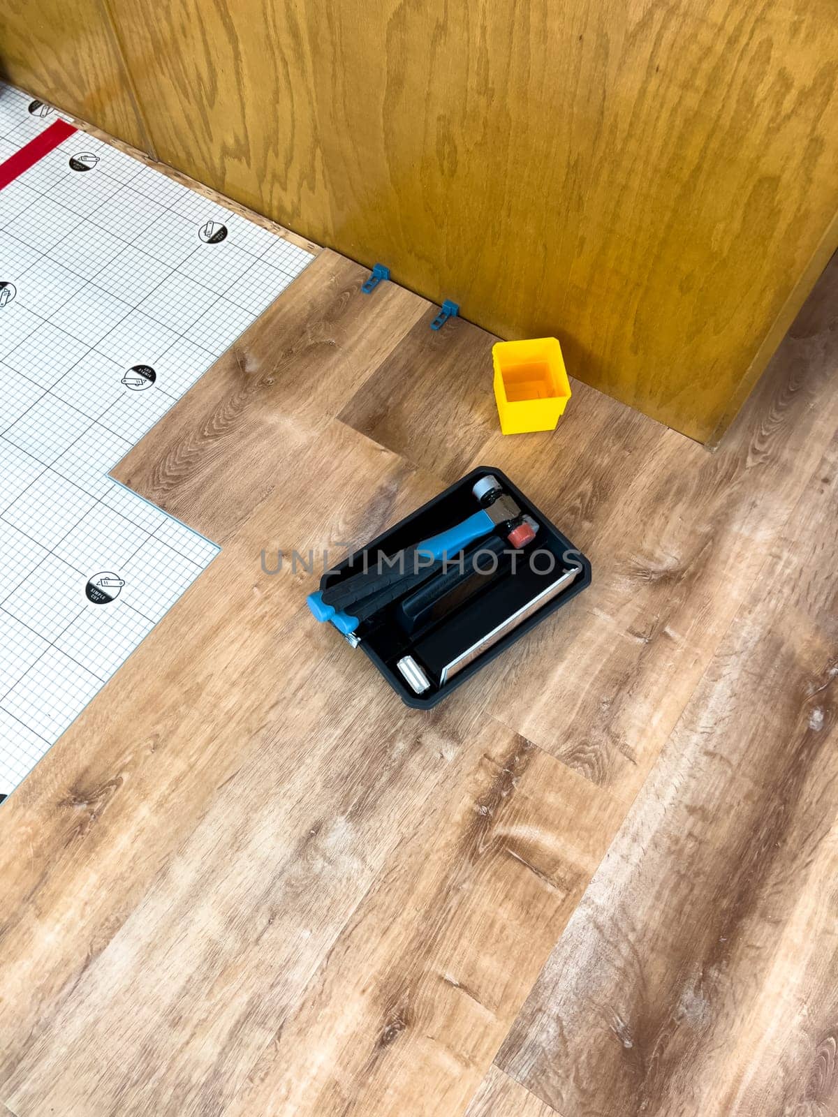 Broomfield, Colorado, USA-February 23, 2025-A close-up of flooring installation tools placed on a newly installed wood-look floor. A tapping block, pull bar, and spacers are visible alongside underlayment, indicating an ongoing home improvement project. The tools are positioned near kitchen cabinetry, highlighting the renovation process.