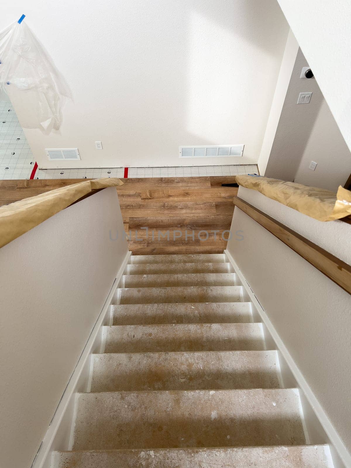 Broomfield, Colorado, USA-February 15, 2025-A staircase under renovation in a home improvement project. The steps remain unfinished, while the upper floor showcases newly installed wood-look flooring. Protective paper is wrapped around the handrails, and construction materials are visible in the background.