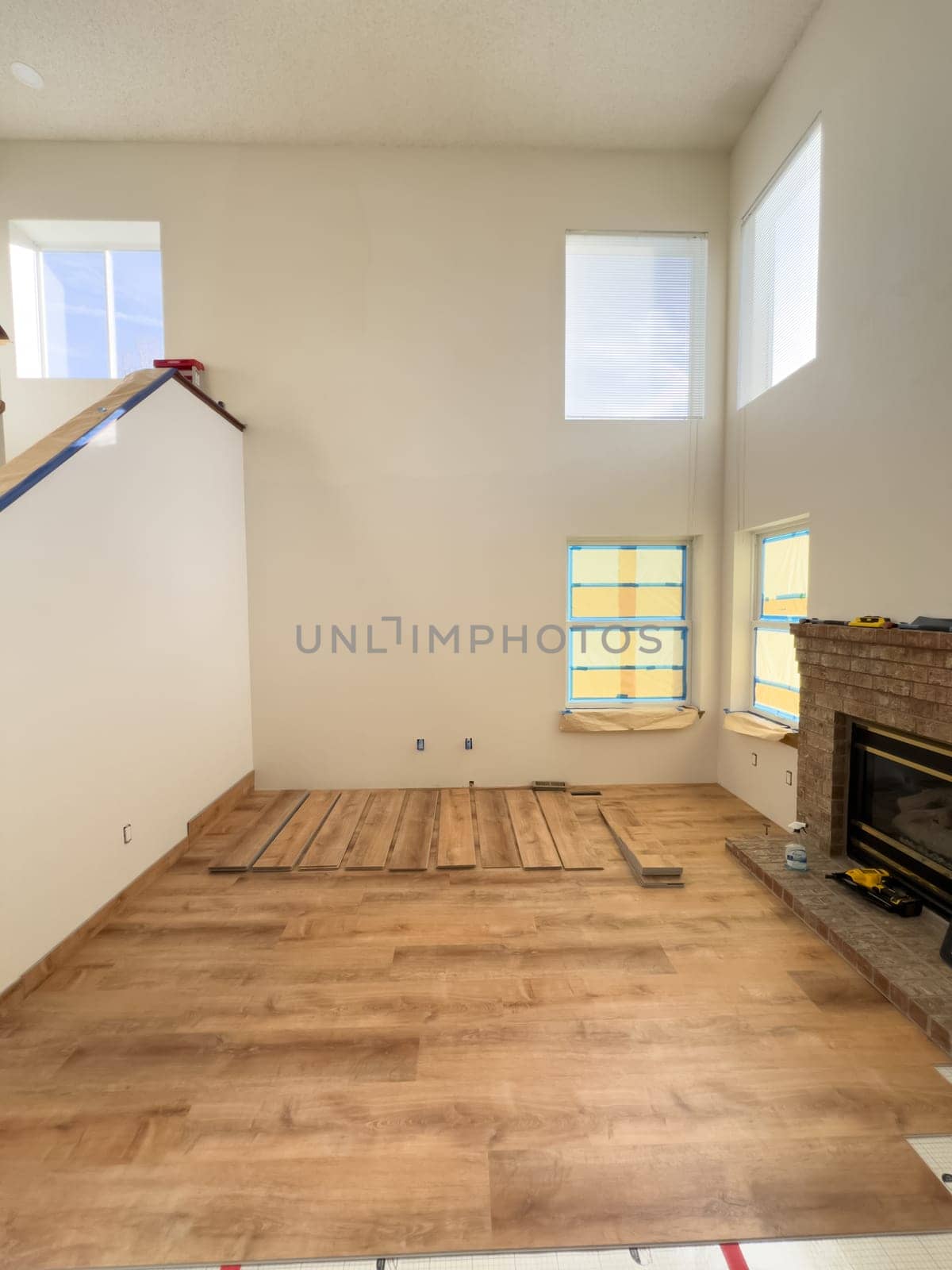 Broomfield, Colorado, USA-January 26, 2025-A spacious living room undergoing flooring installation, featuring wood-look planks partially laid out. The room has high ceilings, large windows covered with protective film, and a fireplace on the right side. Tools and construction materials indicate an ongoing home renovation project.