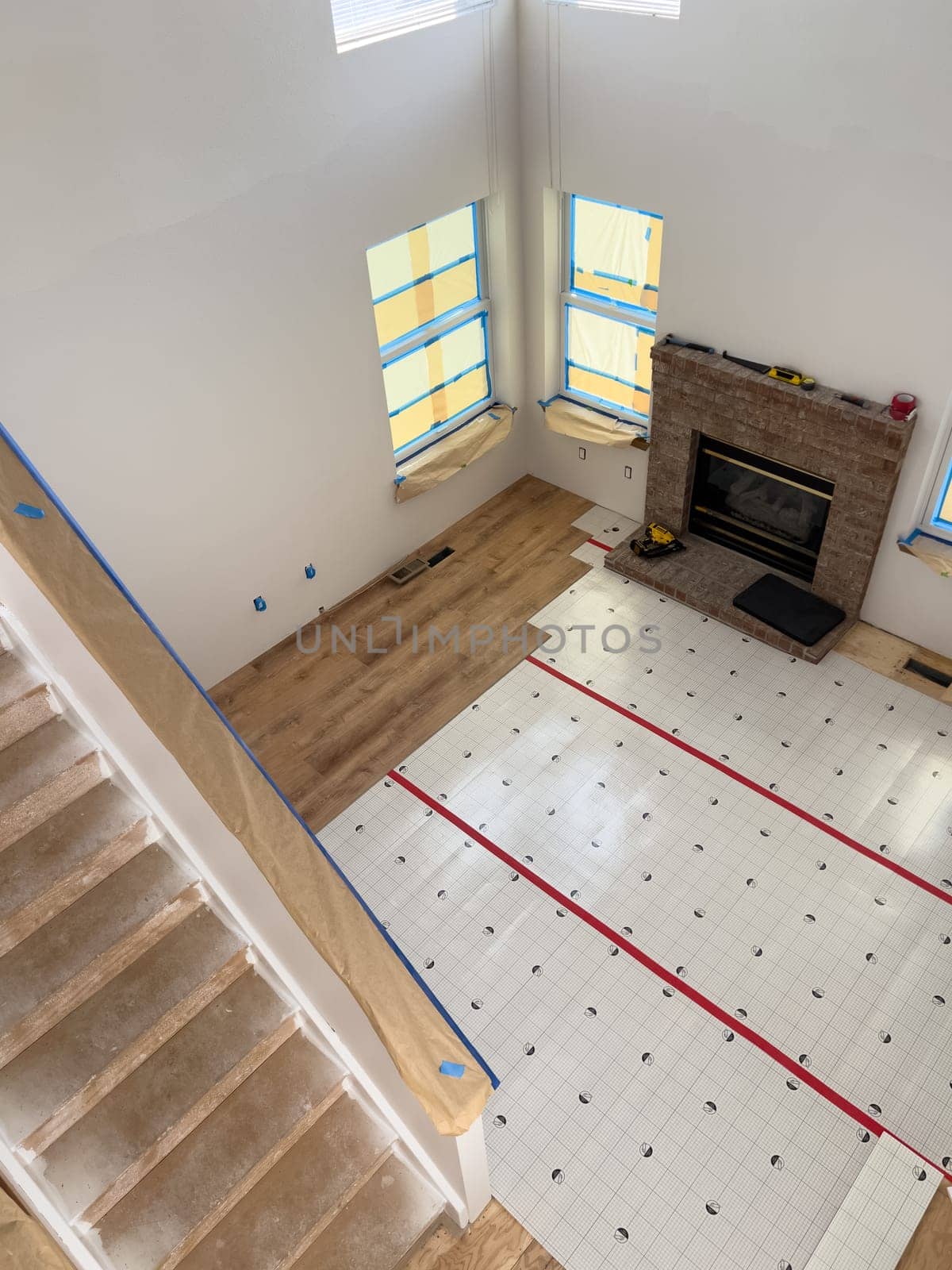 Broomfield, Colorado, USA-January 26, 2025-A spacious living room undergoing flooring installation, with wood-look planks partially laid over an underlayment. The fireplace and large windows bring warmth and natural light to the space. The staircase and walls are prepped for renovation, indicating an ongoing home improvement project.