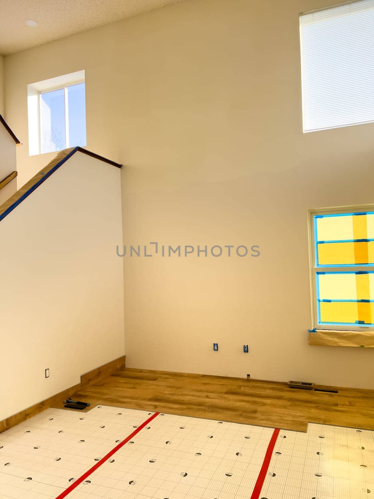Broomfield, Colorado, USA-January 26, 2025-A home interior undergoing renovation with partially installed wood-look flooring. The underlayment is still visible, showing progress in the flooring installation process. The high ceilings, large windows, and staircase add to the spacious and modern feel of the space.