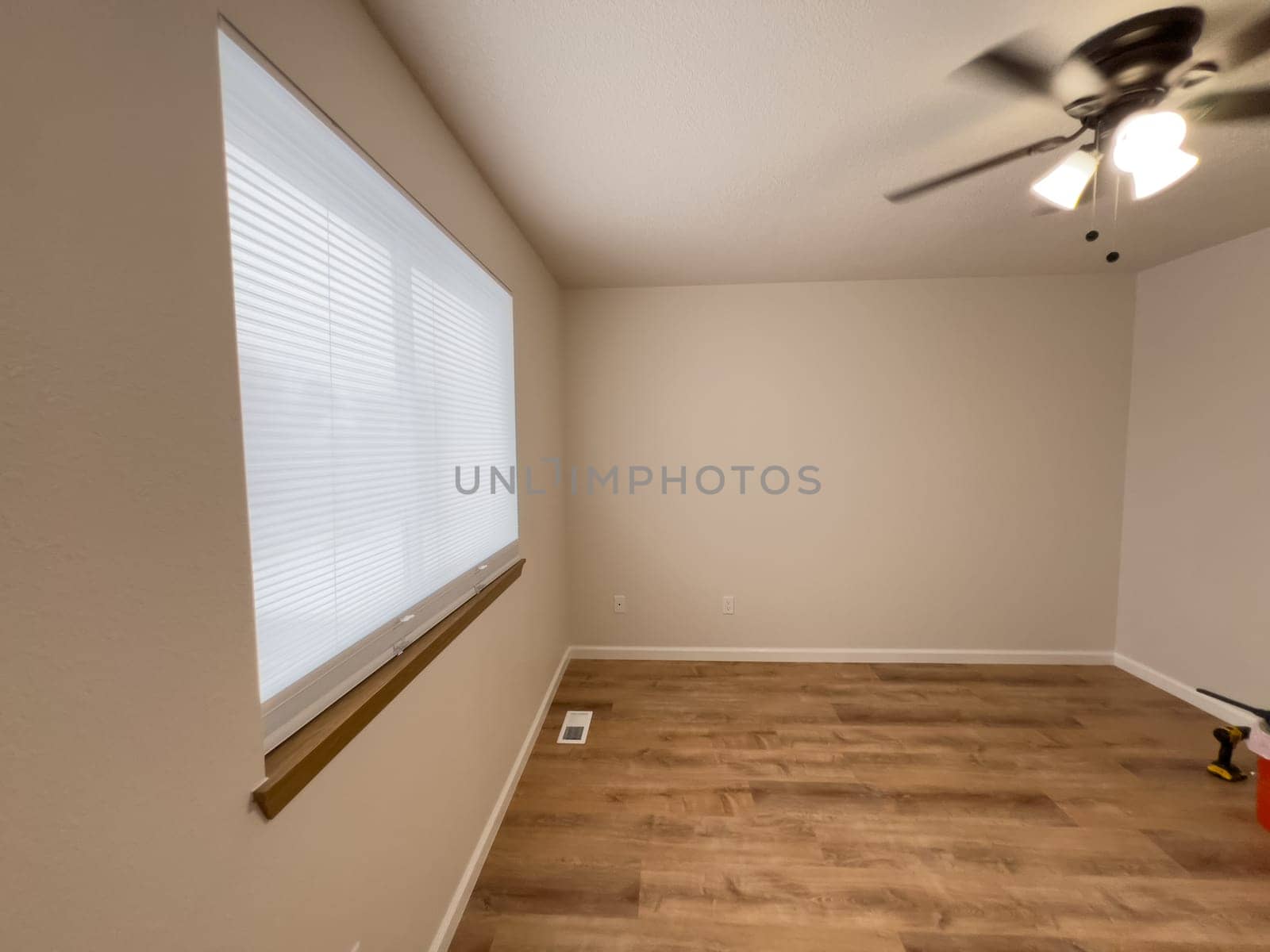 Broomfield, Colorado, USA-January 25, 2025-A freshly renovated bedroom featuring new wood-look flooring, neutral-colored walls, and a ceiling fan with lighting. The large window with blinds allows natural light to brighten the space. A few tools remain, indicating the final touches of the remodeling process.