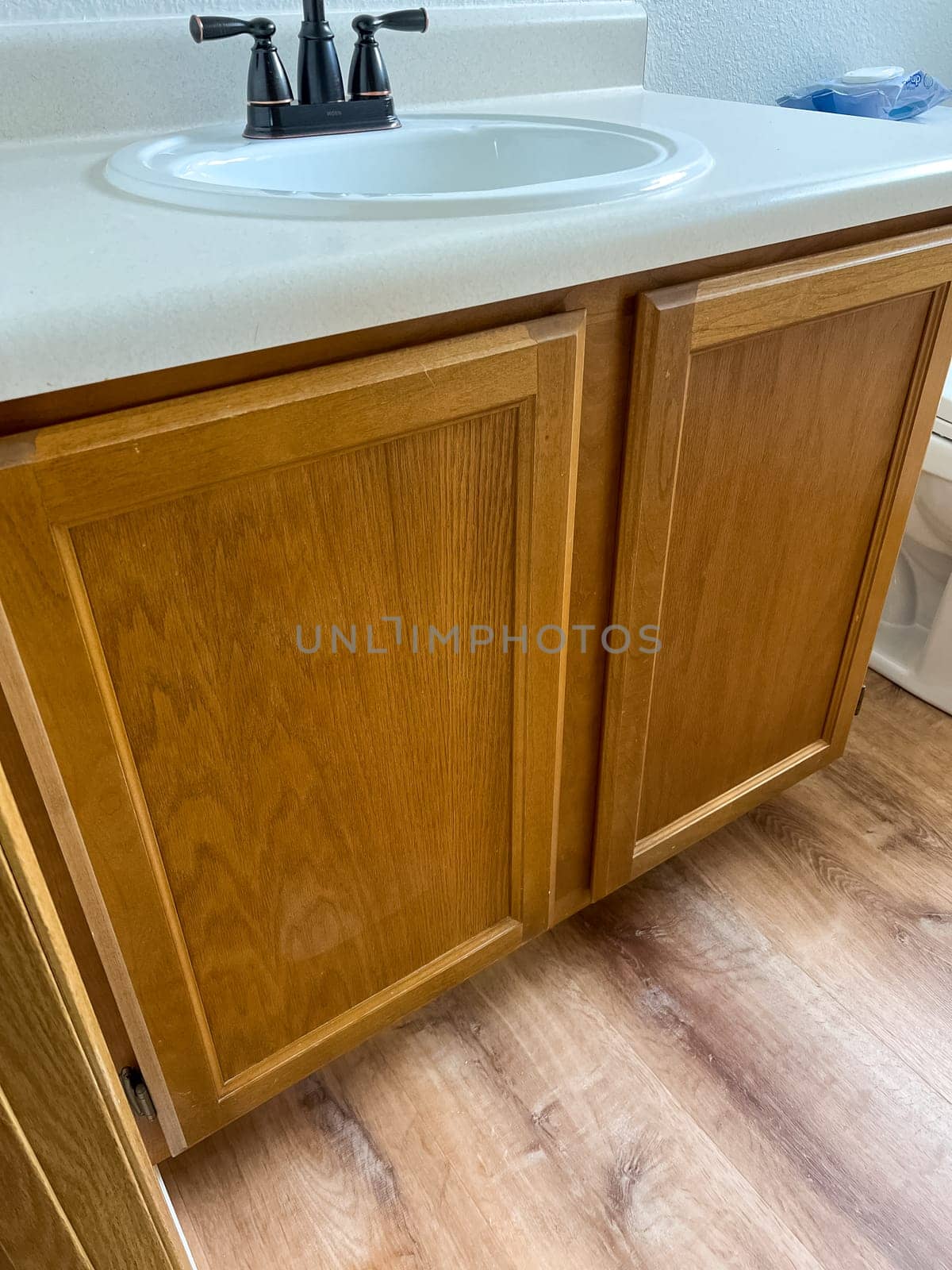 Broomfield, Colorado, USA-January 12, 2025-A close-up view of a wooden bathroom vanity featuring a white countertop, built-in sink, and black faucet. The cabinetry has a natural wood finish, complementing the newly installed wood-look flooring. The vanity adds warmth and functionality to the bathroom space.