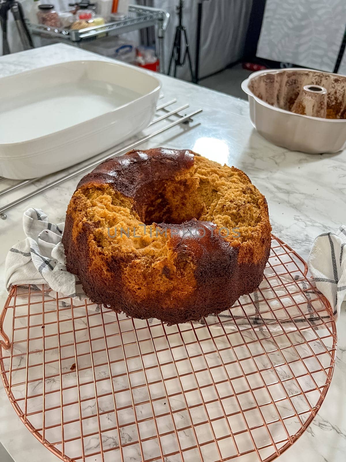 Castle Rock, Colorado, USA-December 31, 2024-A burnt bundt cake sits on a cooling rack in a food photography studio. The uneven texture and overcooked edges suggest a baking mishap. In the background, a bundt pan with cake residue and various kitchen tools are visible, highlighting the process behind the failed bake.