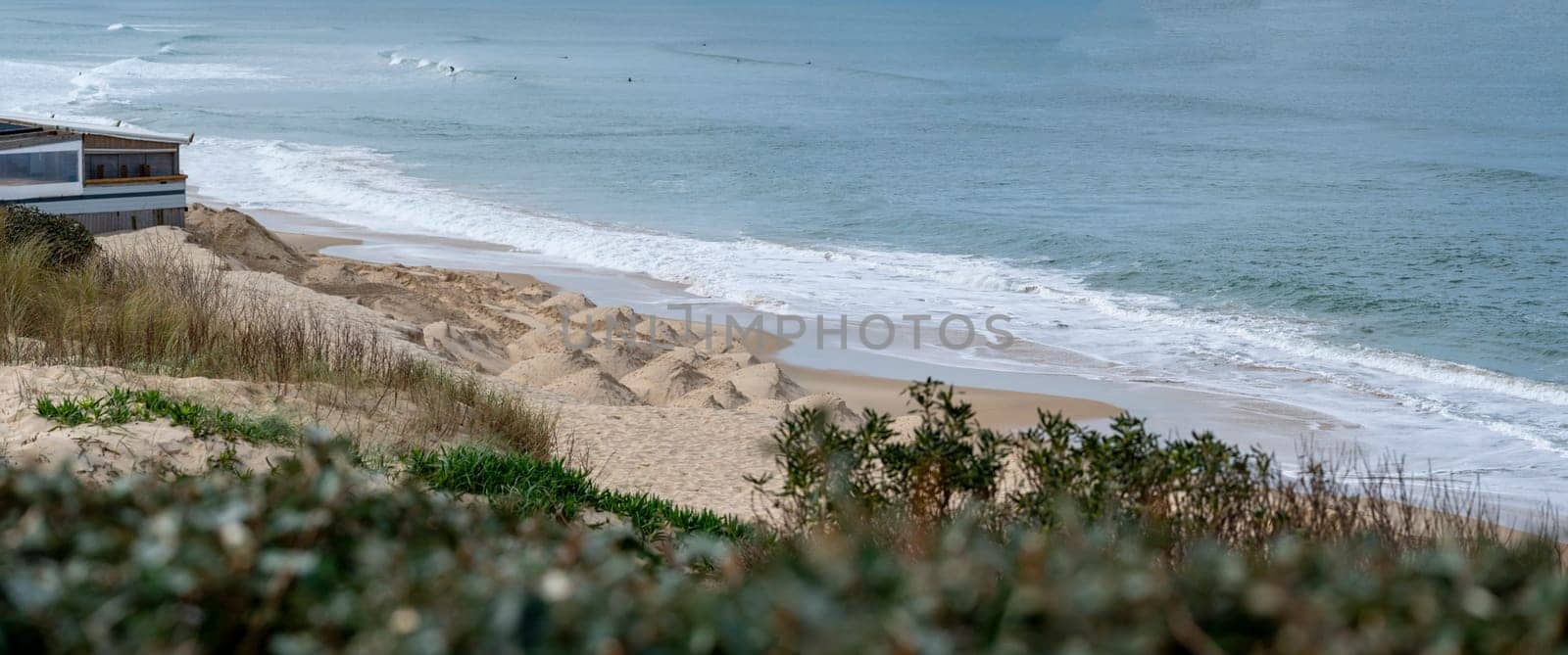 Waves gently lap at the sandy beach of Biscarrosse while soft dunes rise in the background, creating a serene coastal environment on a calm day.