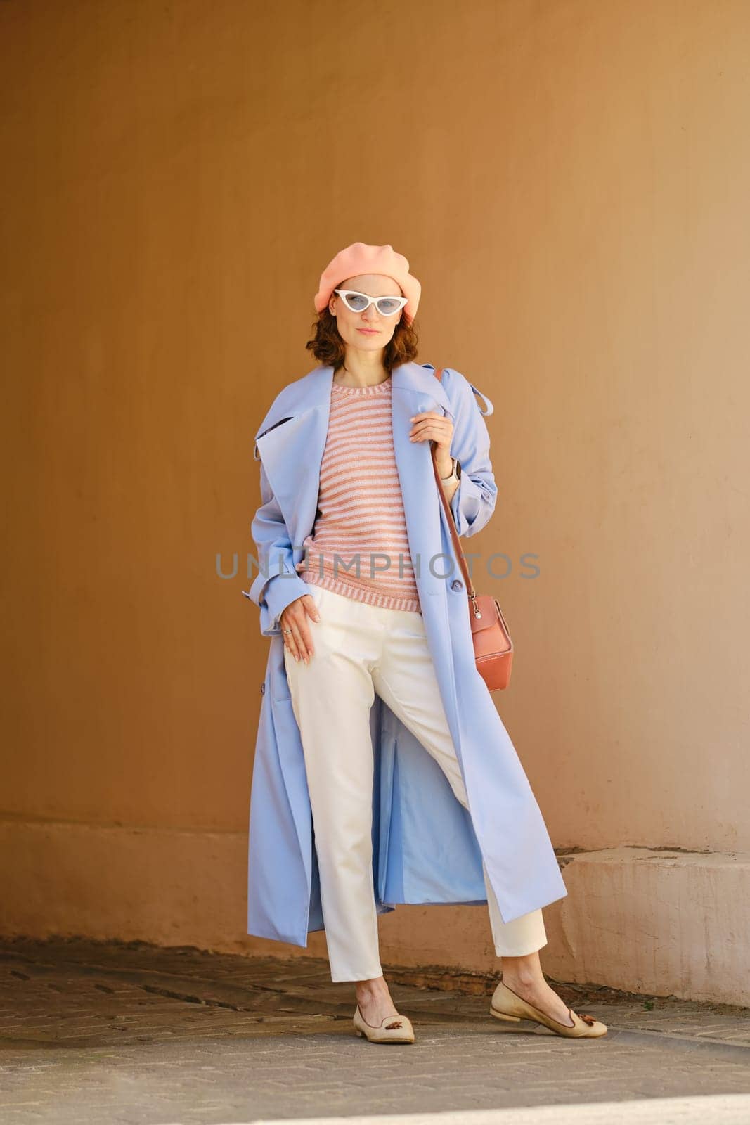 Stylish woman in long trench, breeches and hat standing in arch