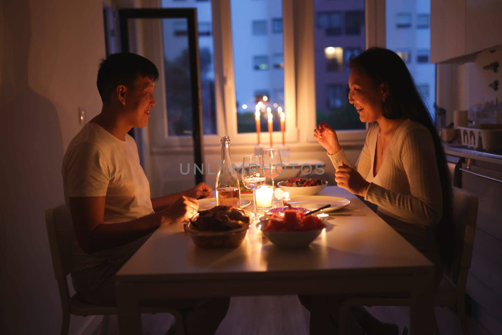 Asian couple having romantic evening meal by candlelight in their apartment