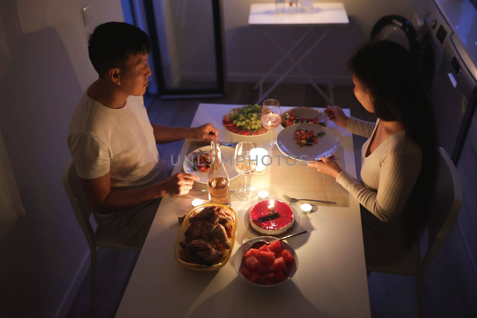 Young couple having romantic candlelit dinner with roasted chicken, cake, salad, and fruit