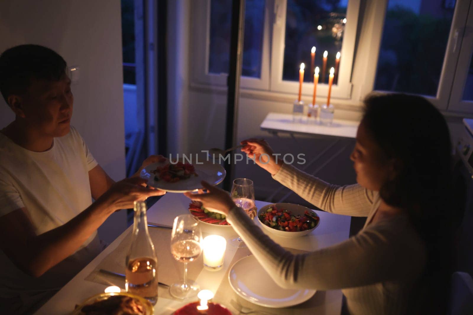 Young couple enjoying a romantic candlelit dinner at home, sharing food and creating a warm atmosphere