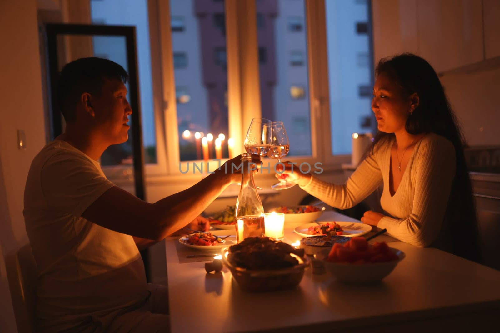 Young couple enjoying a romantic candlelit dinner at home, toasting with wine glasses