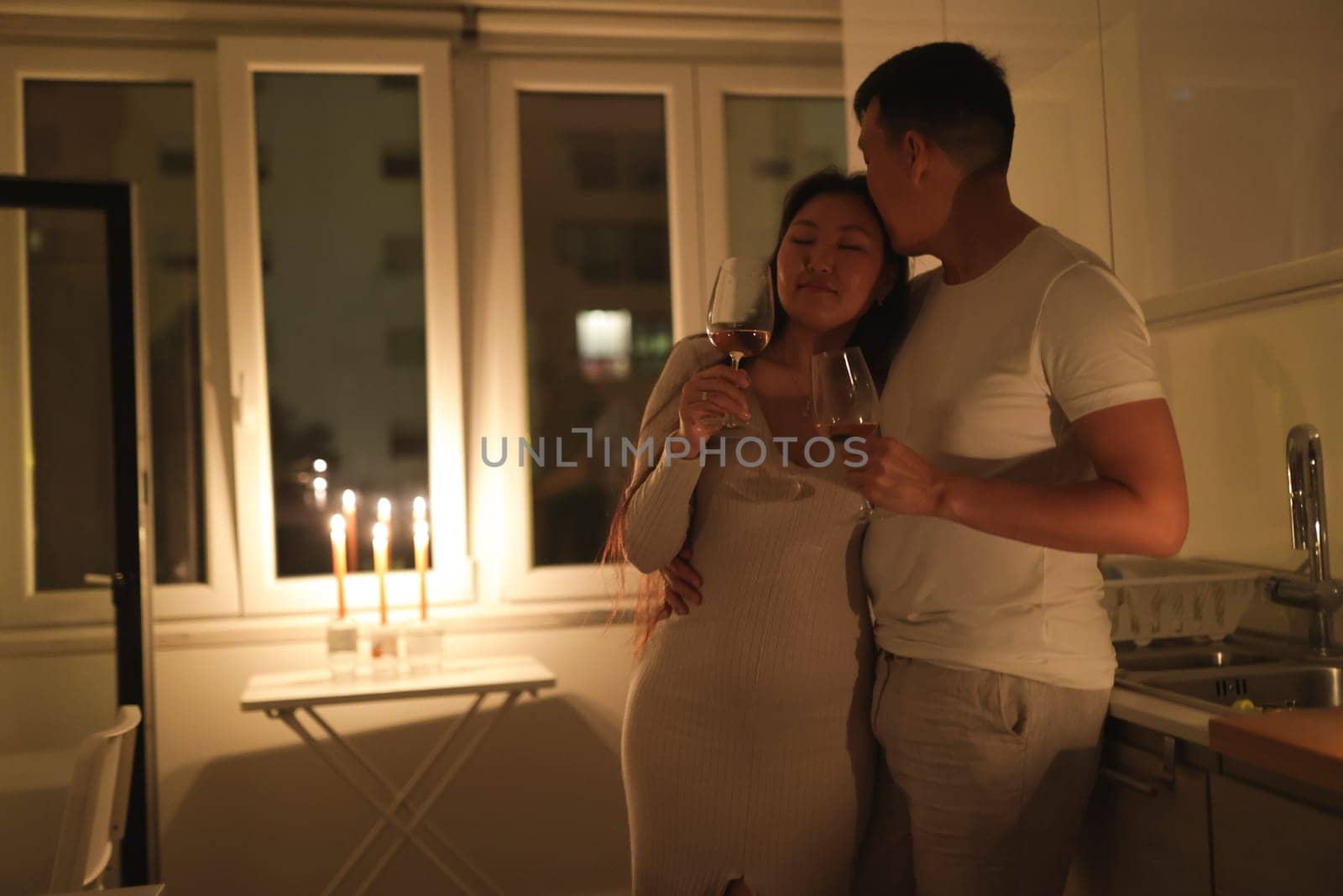 Couple embracing and drinking wine in a candlelit kitchen, creating a romantic and intimate atmosphere