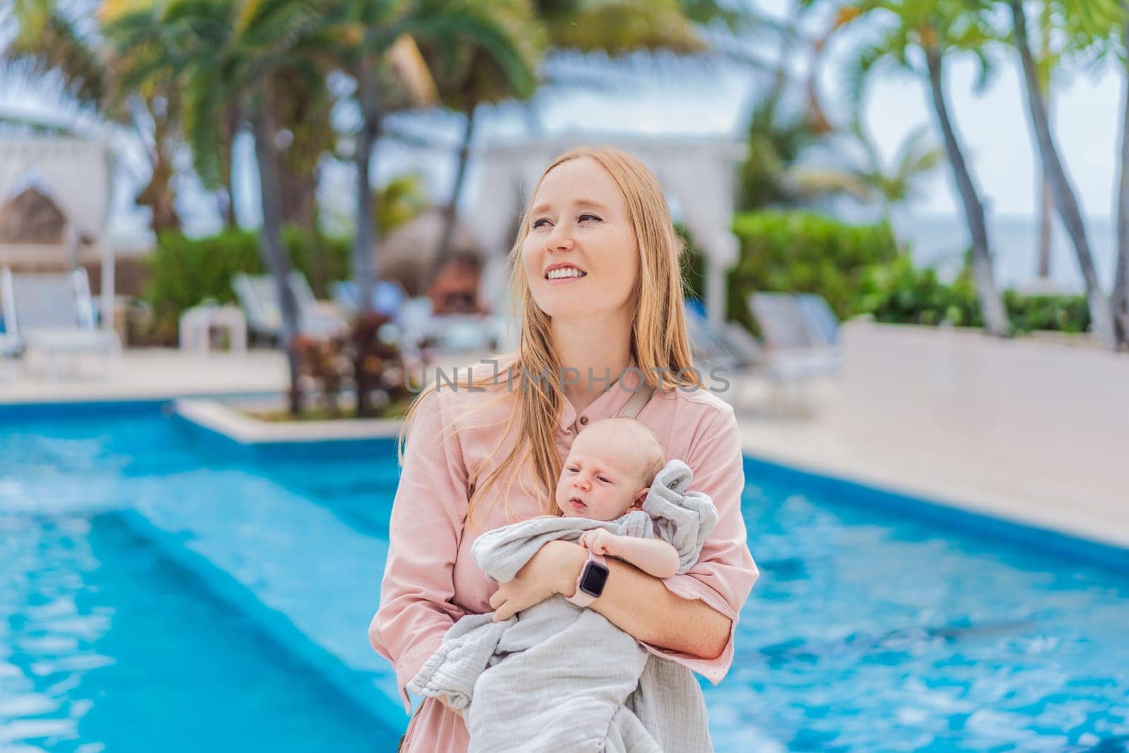 A mother holds her baby near a tropical pool, surrounded by lush greenery. This heartwarming moment captures family bonding, maternal love, and the serene beauty of a tropical getaway, perfect for relaxation and connection.