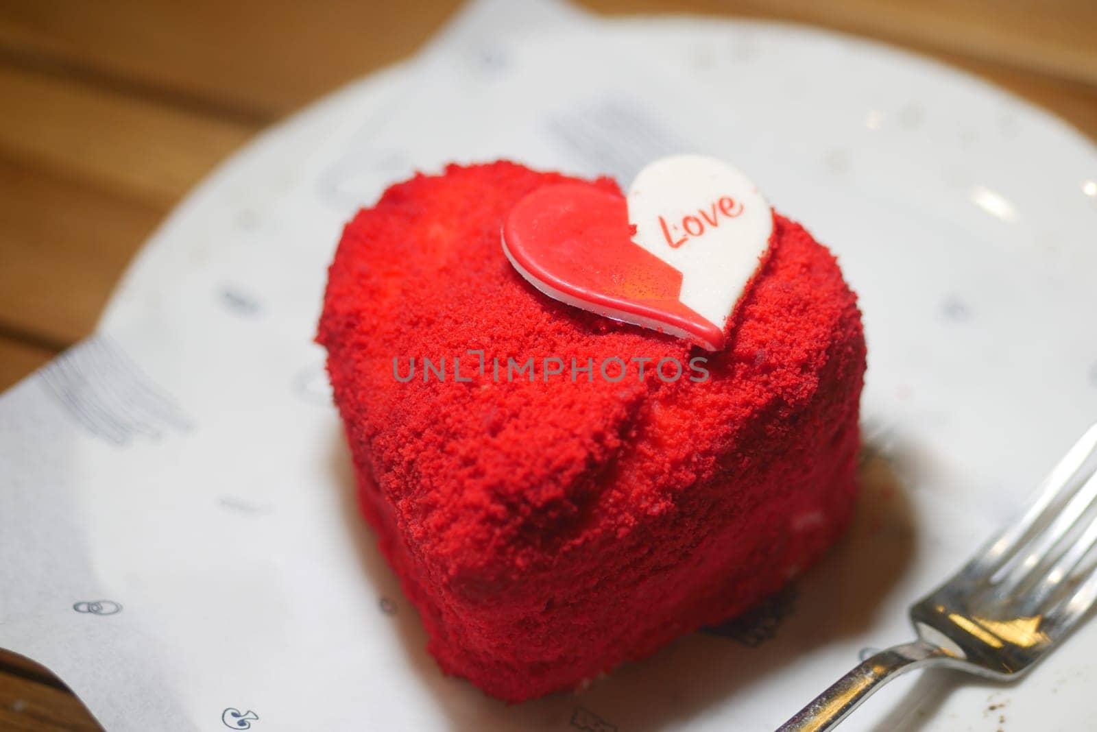 A vibrant red heart-shaped cake topped with a love sign sits on a plate.