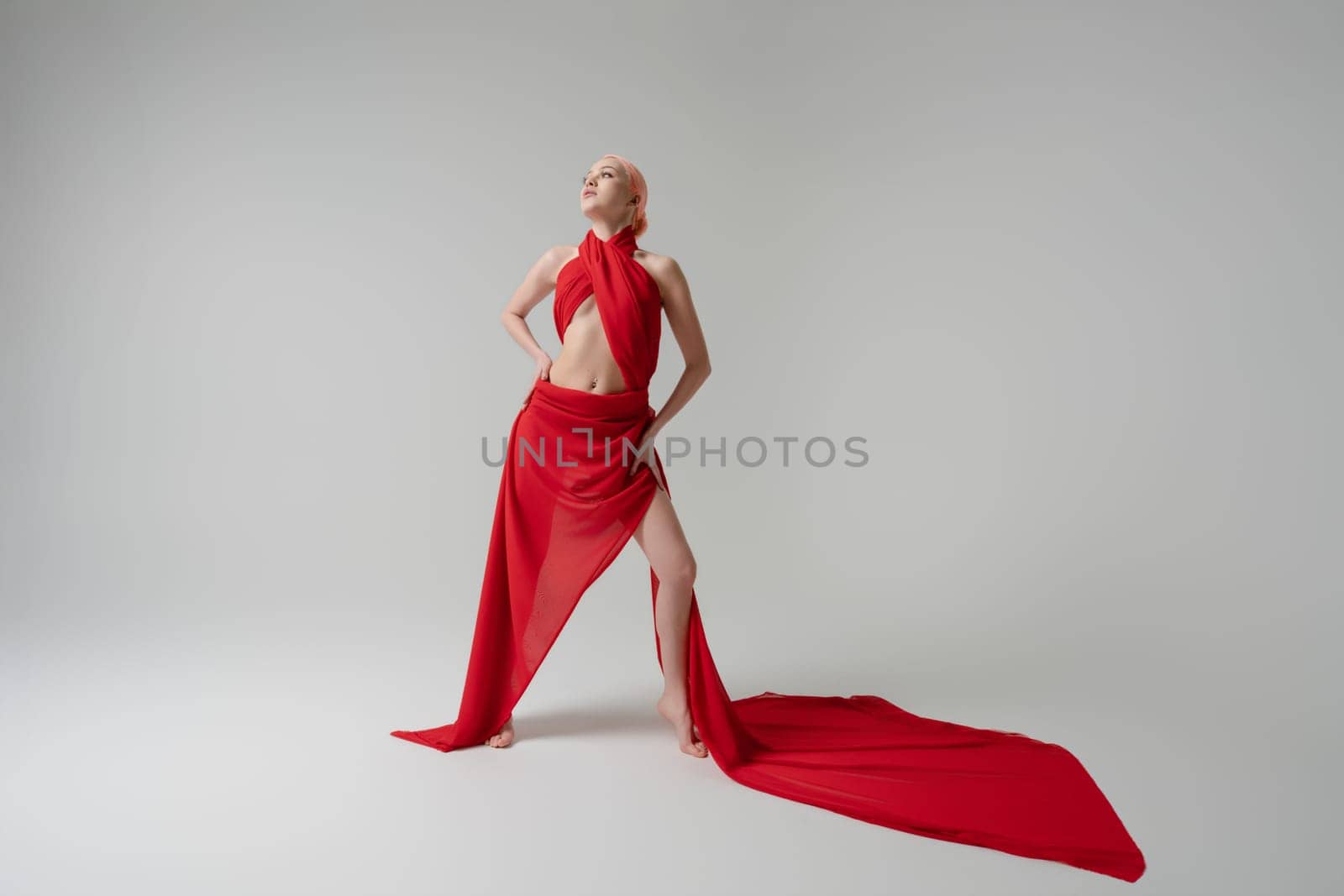 A woman stands confidently, adorned in flowing red fabric that accentuates her beauty and grace in a well-lit studio setting.