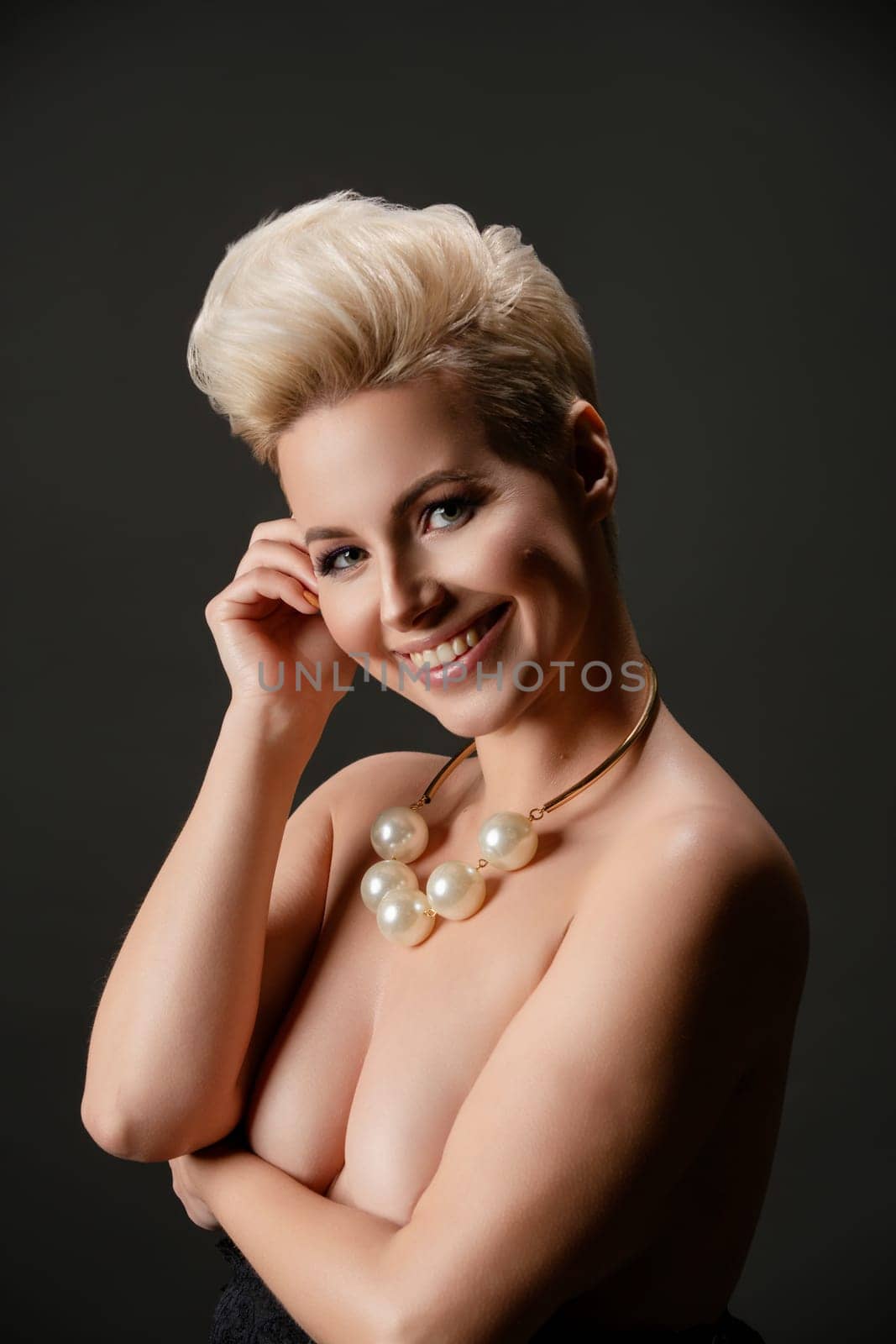 A confident woman poses topless with striking accessories, exuding beauty and elegance against a dark backdrop.