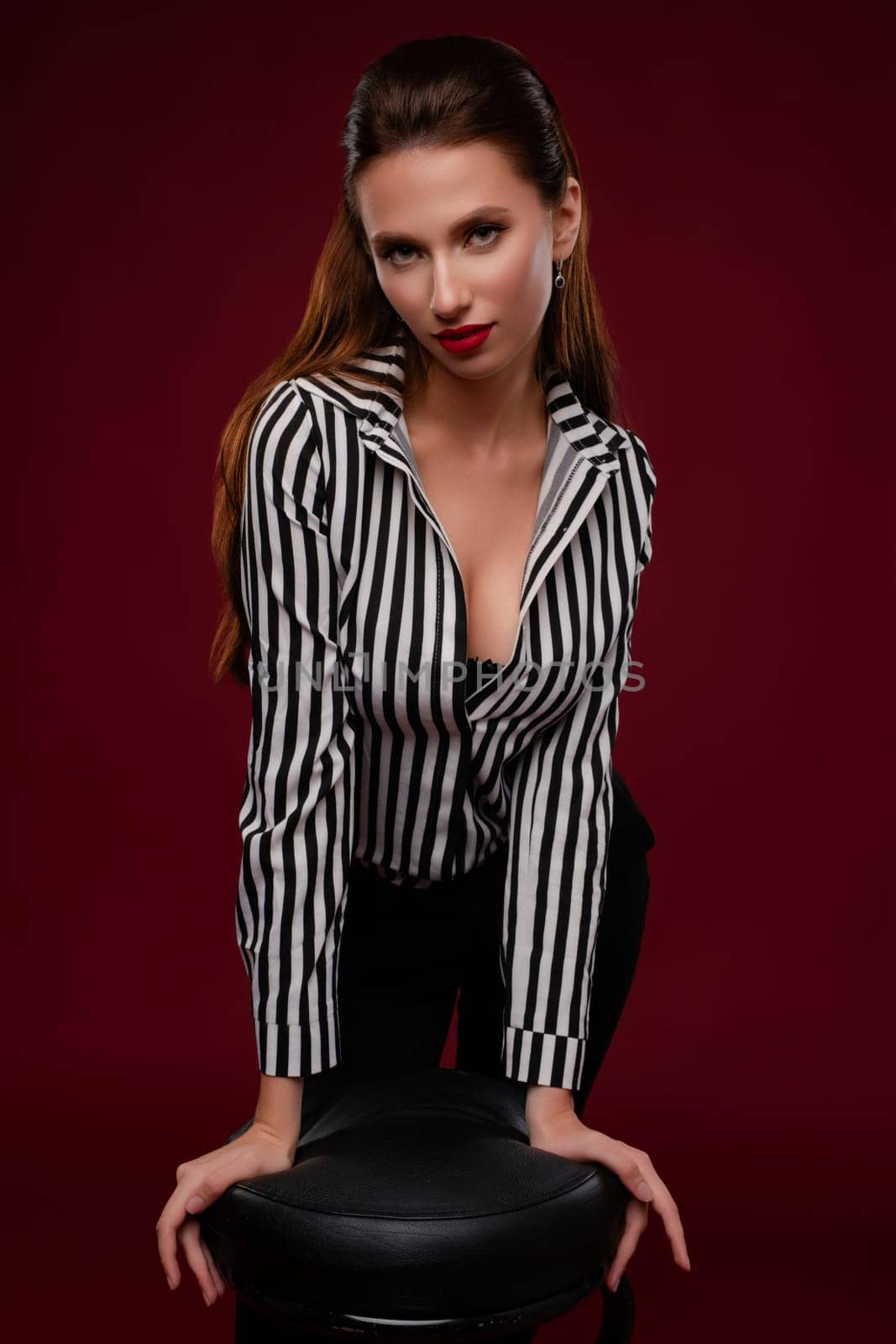 A confident woman showcases her beauty in elegant lingerie while posing in a studio with a rich background.