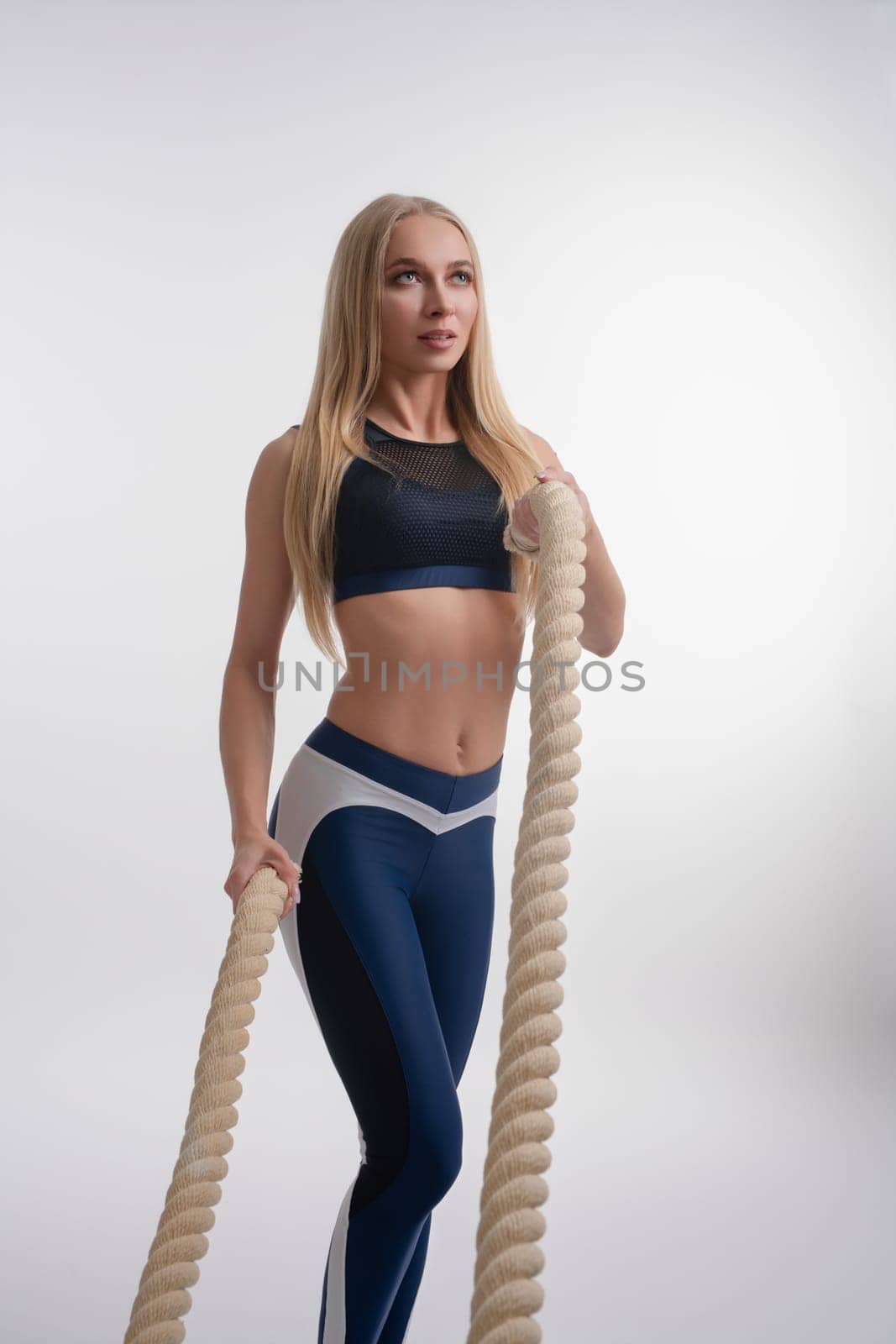 A female athlete performs an intense workout with ropes, showcasing strength and grace in a studio environment.