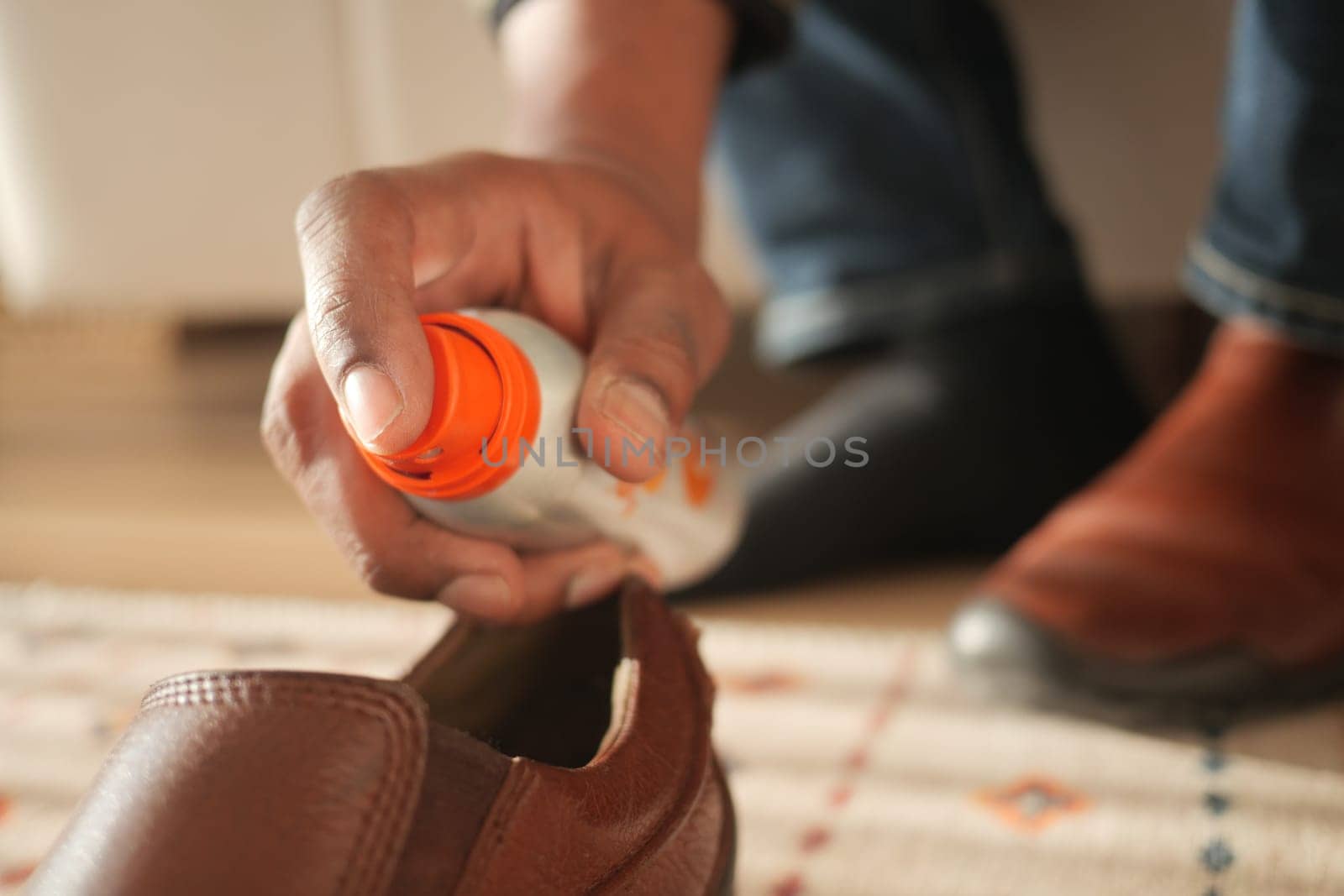 A person is treating brown leather shoes with a care product indoors.