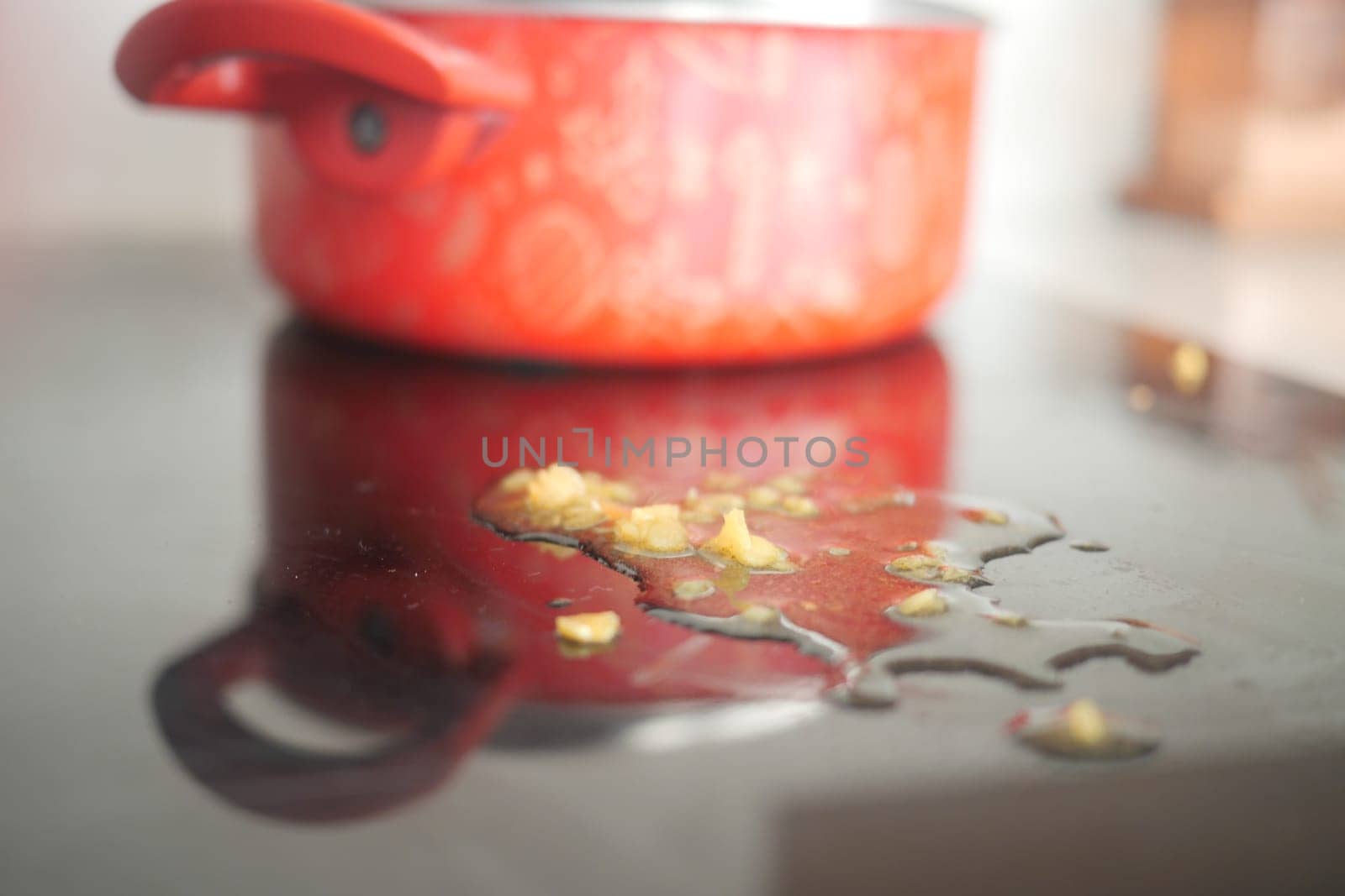Oil is spilled on a countertop beside a red pot after cooking.
