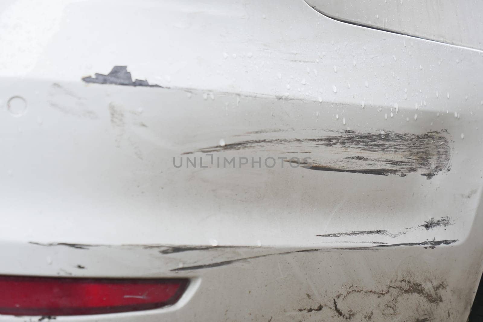 Bumper of a white car showing scratches and damage from an accident.