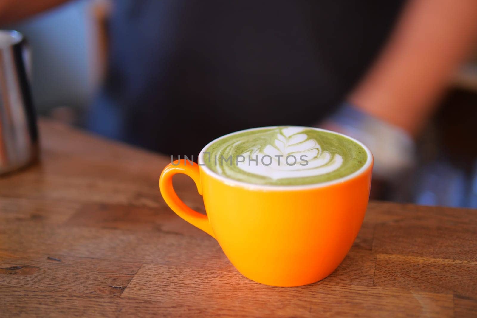 Delicious matcha latte served in vibrant orange cup on wooden table,