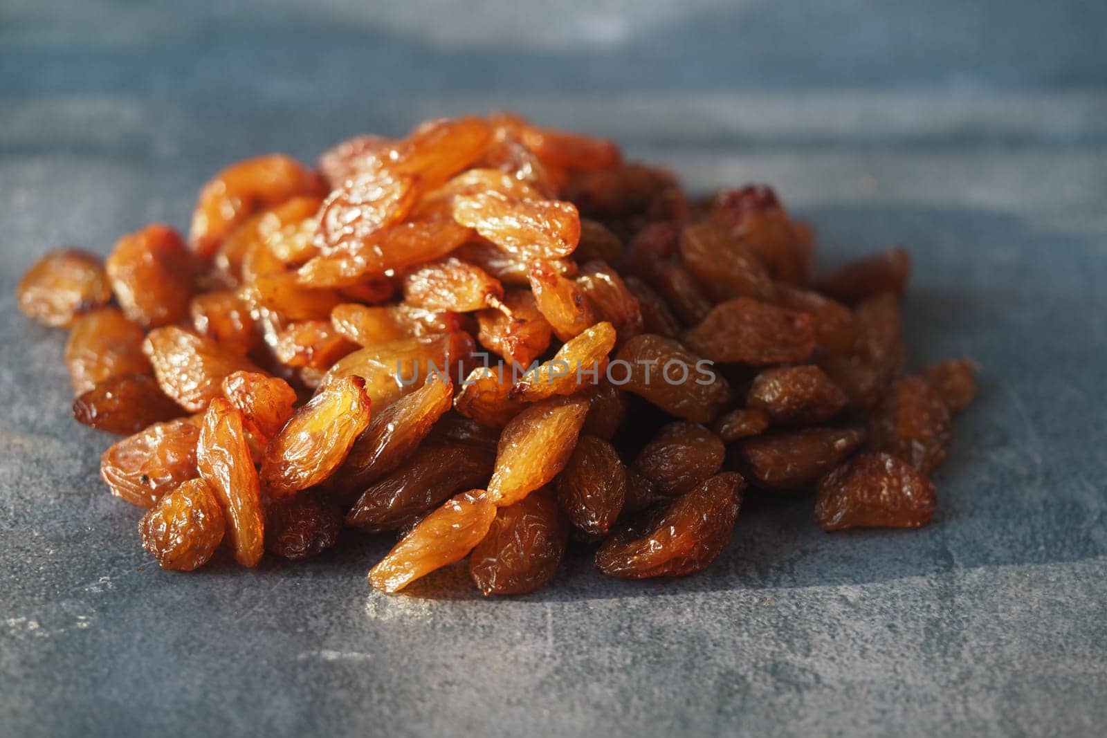 A pile of golden raisins rests on a textured surface with bright lighting.