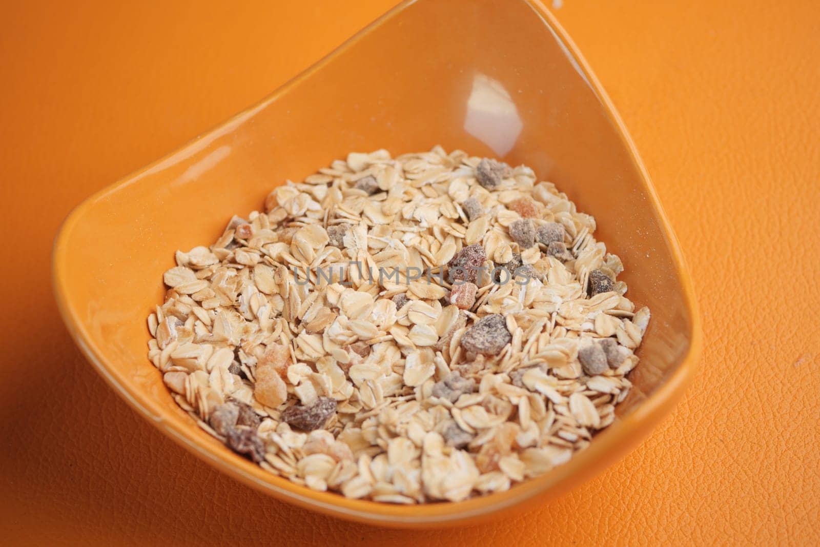 Bowl containing oats mixed with various dried fruits on an orange surface.