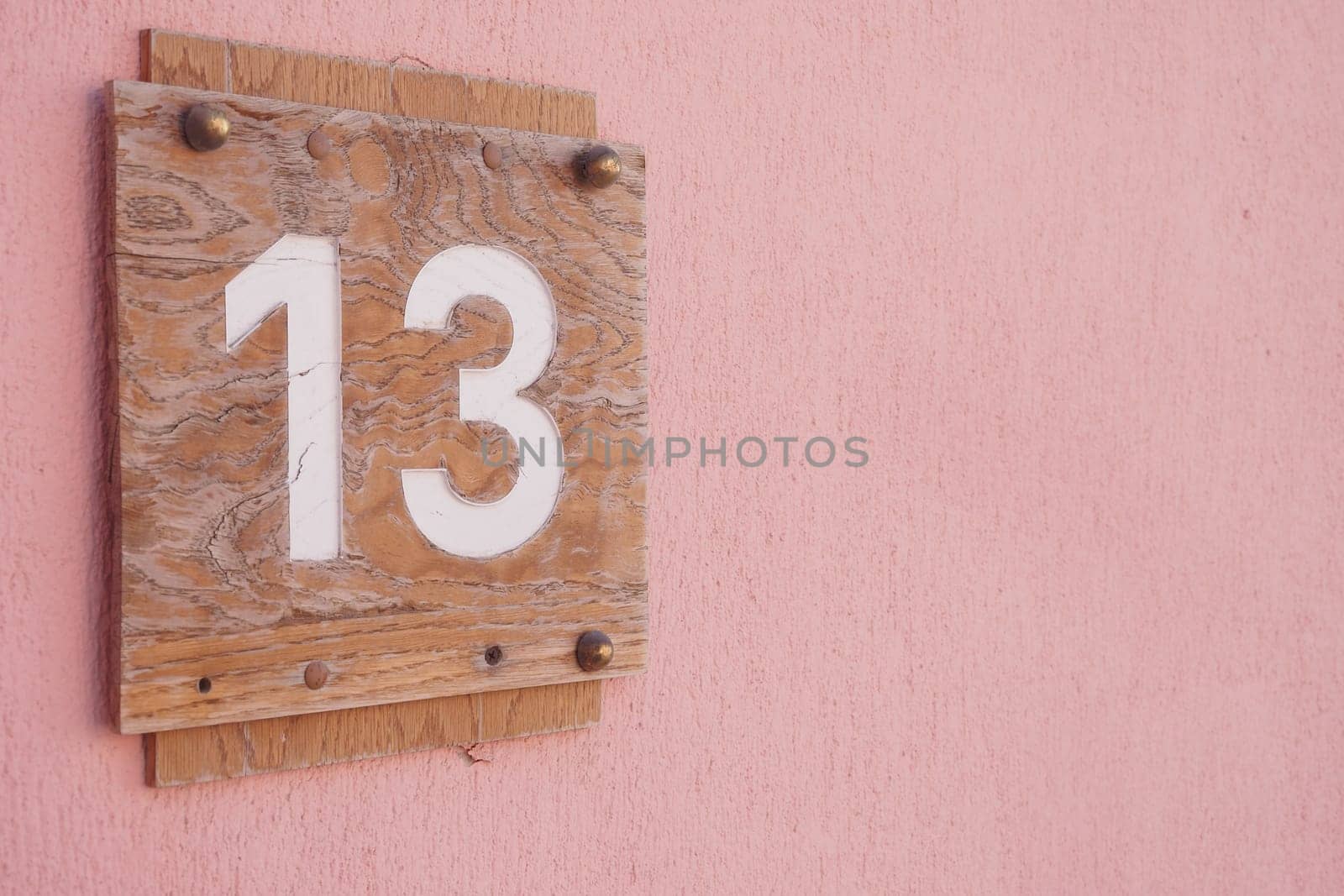 A weathered wooden sign displays number 13 against a pink wall.