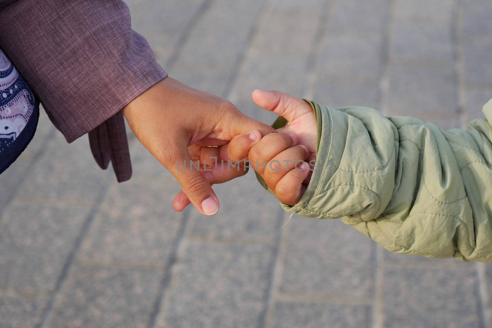 An adult and a child hold hands while walking along a plaza.
