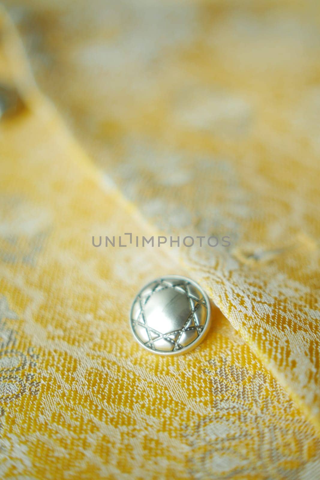 Silver button shines on textured yellow fabric, creating a captivating contrast.
