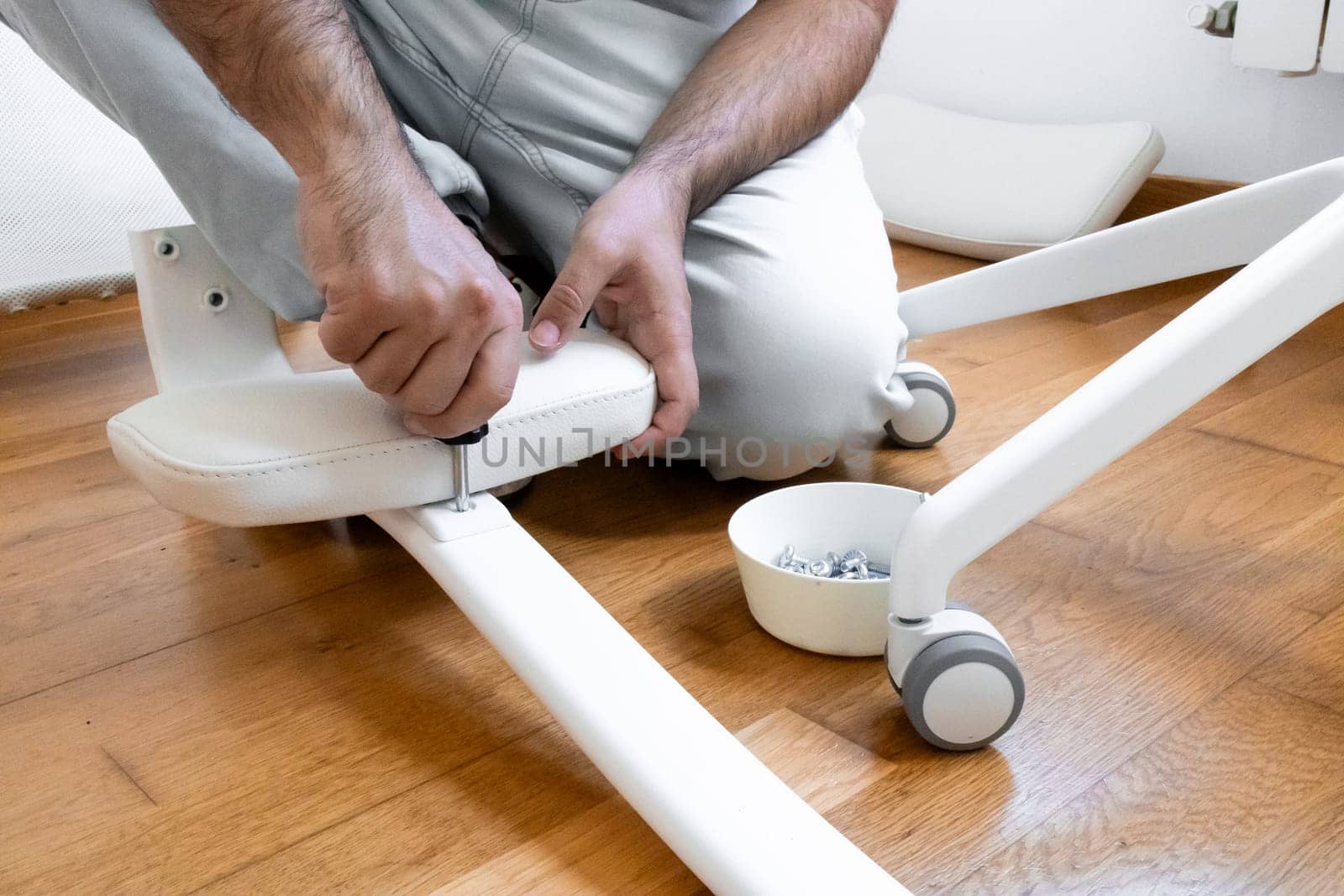 Caucasian male assembling white office chair on wooden floor.