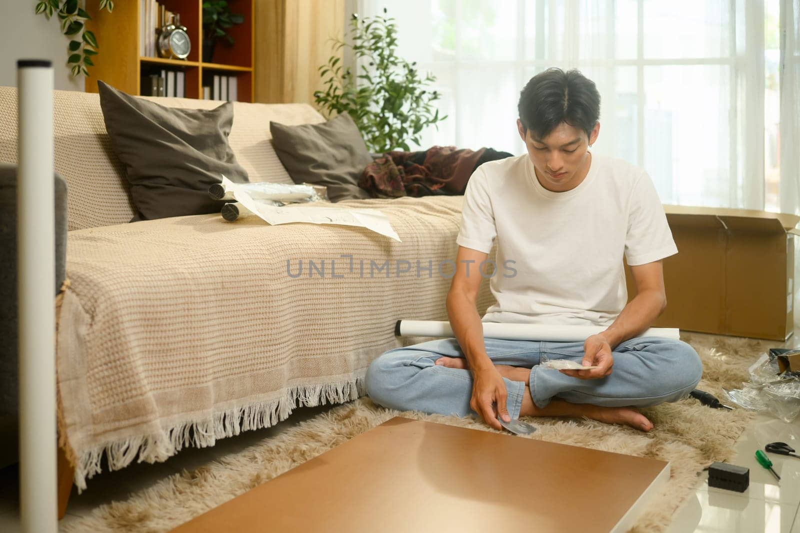 Focused asian man assembling a piece of furniture. Home organization and interior decorating concept.
