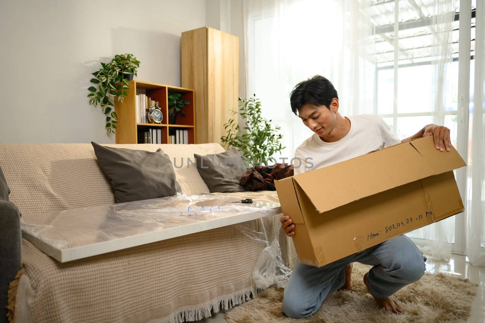 Smiling young man unpacking and assembling a piece of furniture in a living room.