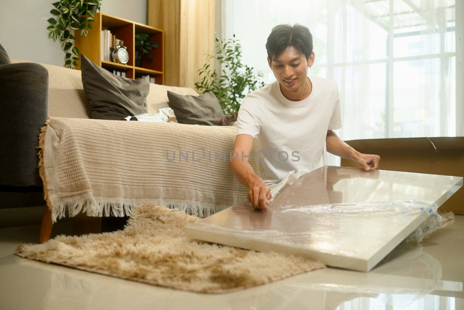Smiling young man unpacking and assembling a piece of furniture in a living room.