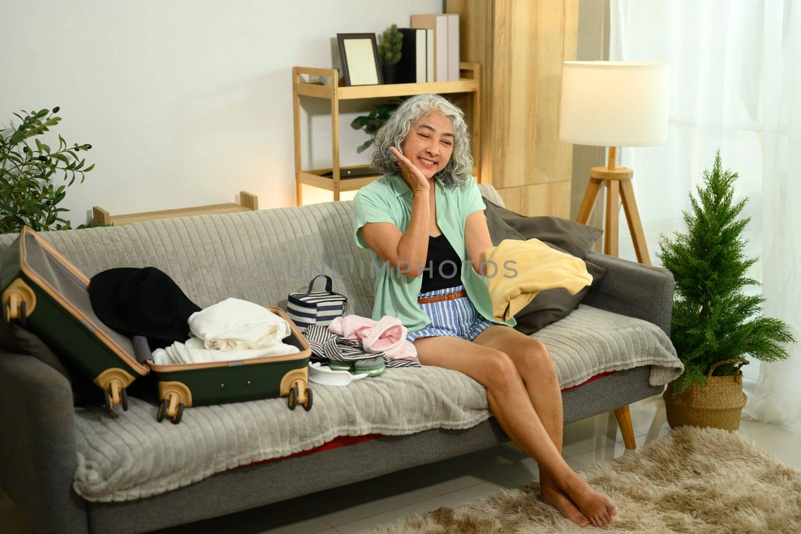 Happy senior woman packing clothes for a summer vacation.