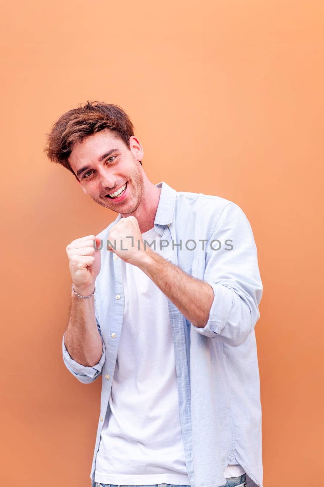 man standing in front of orange wall making a fist and smiling happy, concept of success and happiness