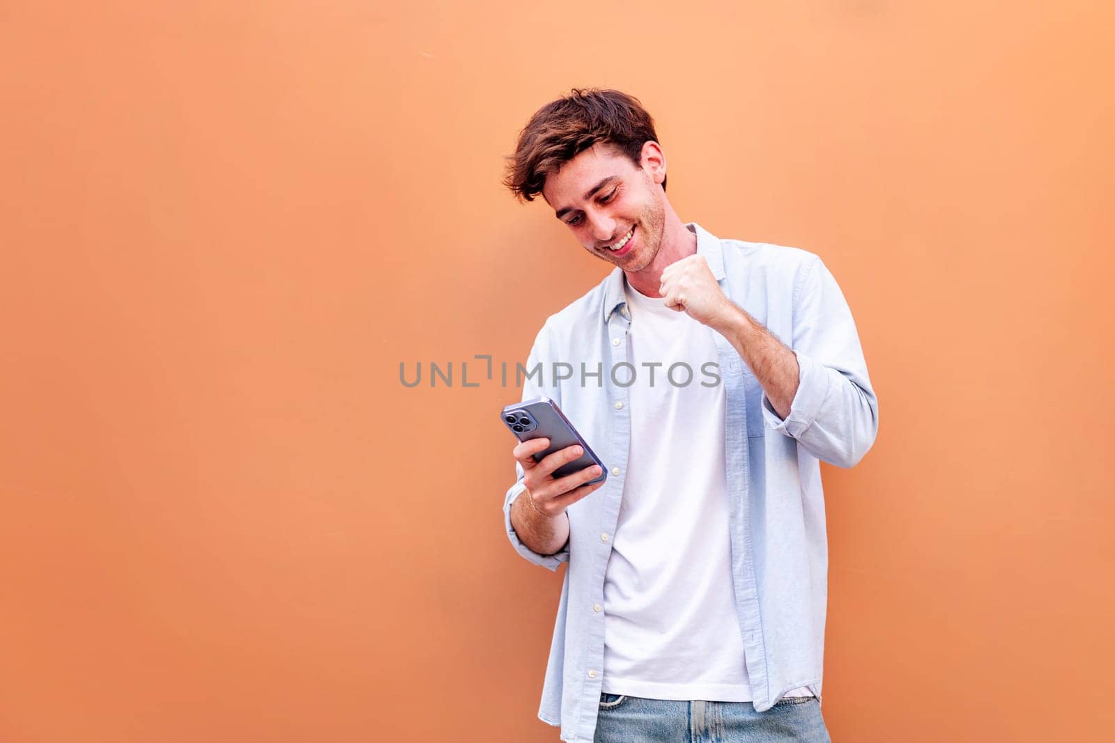 young man holding cell phone and smiling happy while celebrating , concept of positivity and enjoyment of technology, copyspace for text