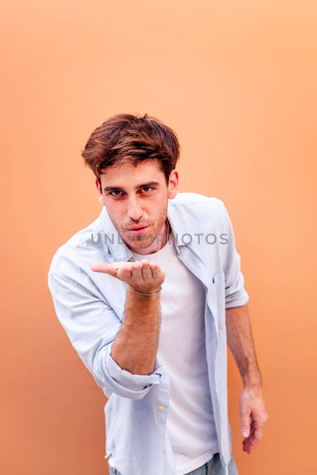 young man giving a kiss with hand while smiling looking at camera in a positive and friendly mood, concept of love, copyspace for text