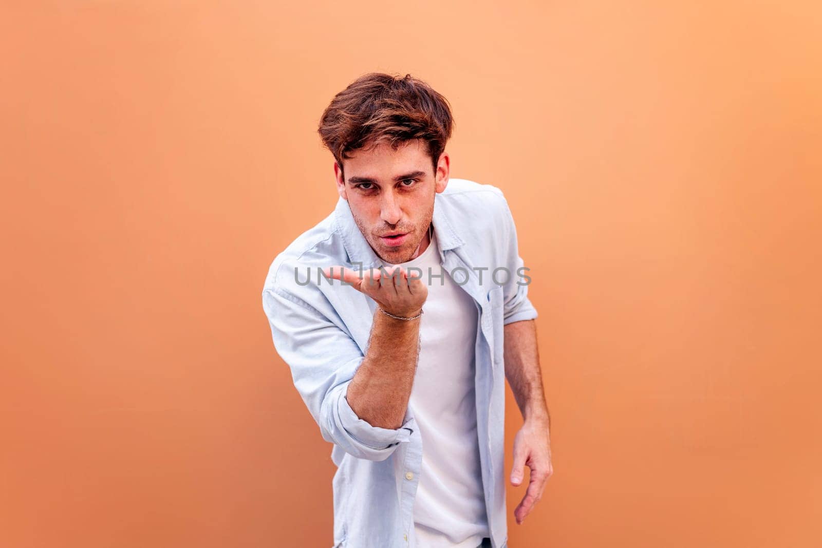 young man giving a kiss with hand while smiling looking at camera in a positive and friendly mood, concept of love, copyspace for text