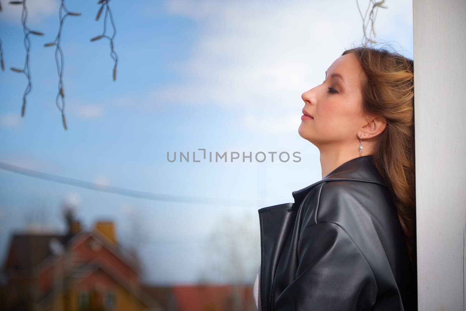 A woman leans against a pillar, closing her eyes peacefully as she savors the warm sunlight and fresh air.