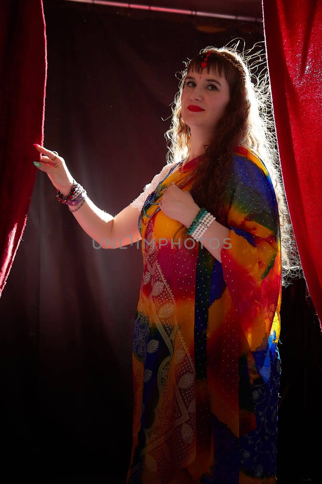 A mature woman in a colorful sari poses elegantly, showcasing her style and confidence during a creative Indian-themed shoot.